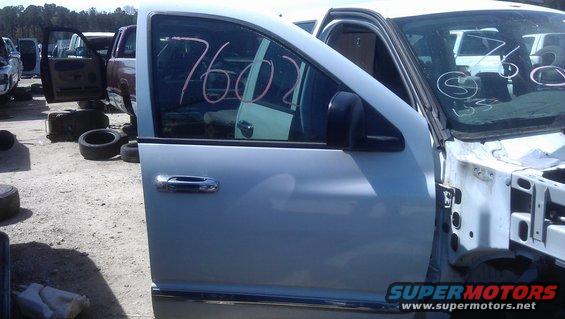 Light-colored truck door with pink numbers '7602' written on the window, parked in a junkyard with other vehicles and tires