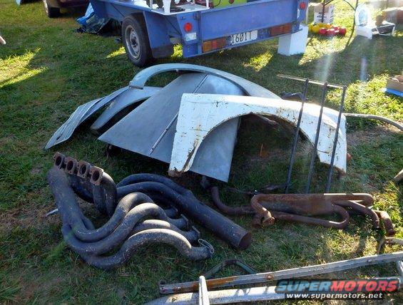 Exhaust headers and car fenders piled on grass near a trailer