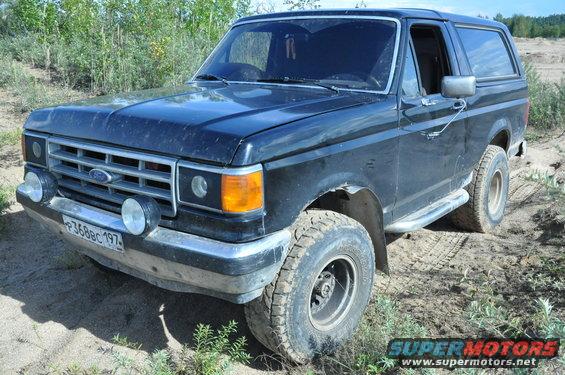 Black 1987 Ford Bronco parked on a dirt road with vegetation