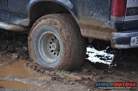 Mud-covered 1987 Ford Bronco rear tire stuck in mud, with visible Ford badge