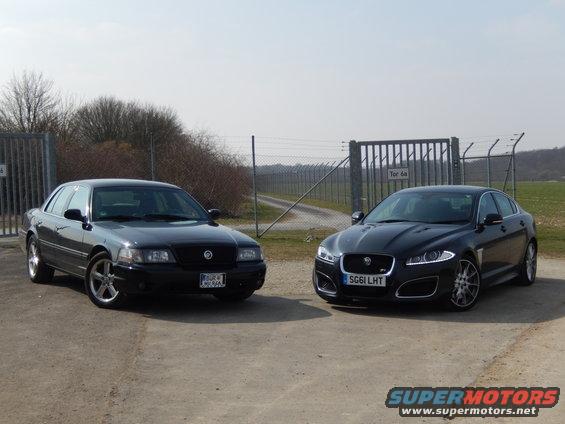 Black Mercury sedan and black Jaguar sedan parked side-by-side in front of a fence and gate