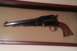 2003 Ford Crown Victoria - A black revolver with a wooden grip is mounted against a tan backing, framed by dark wood.