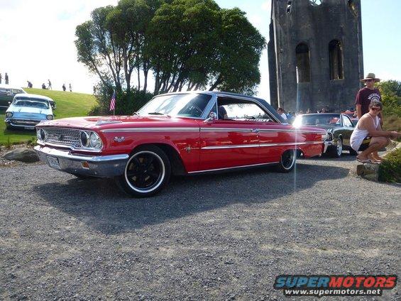 Red 1963 Ford Galaxie 500 parked near a stone tower. Another car is behind it