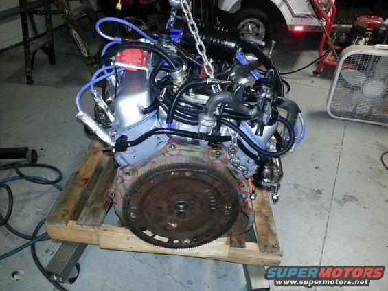 Engine on wooden pallet, suspended by chains, with visible flywheel and red distributor cap