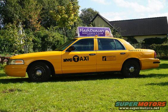 Yellow 2006 Ford Crown Victoria taxi with NYC T Taxi markings and a Flashdancers sign