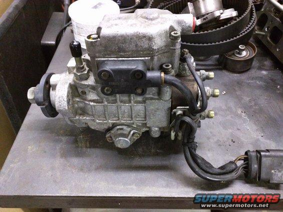 Diesel fuel injection pump on a workbench with a timing belt in the background