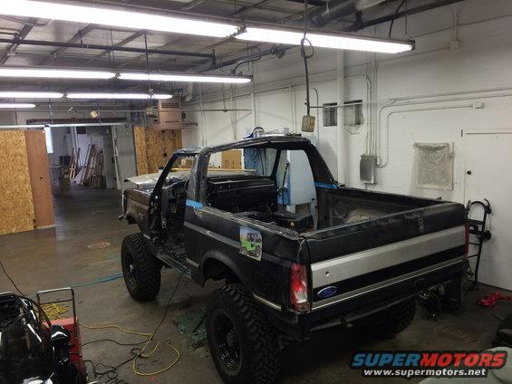 Black Ford Bronco with roof removed, undergoing repairs in a garage
