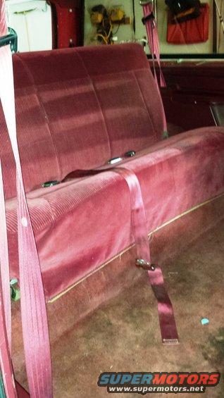 Maroon velour bench seat with pink seatbelts, viewed from the side