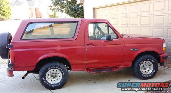 Red 1994 Ford Bronco parked in driveway, side view. Spare tire mounted on rear