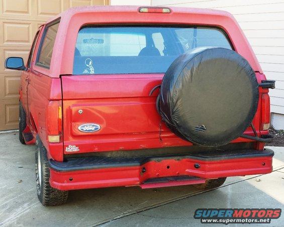 Red Ford Bronco rear view, spare tire mounted externally, black bumper, garage door in background