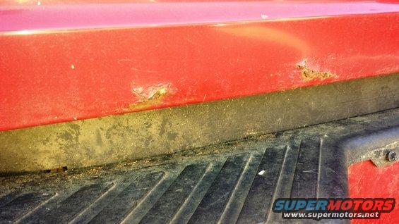 Red truck bed corner with rust and black plastic trim