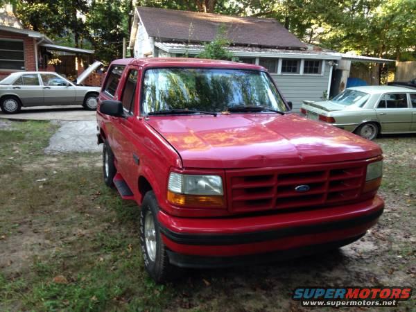 Red Ford Bronco parked in a yard with a silver Mercedes-Benz and another light-colored sedan in the background