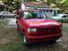 2001 Ford F-150 - A red Ford Bronco is parked in a grassy area next to a house, with other vehicles visible.