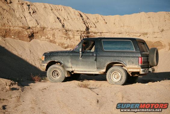 Black Ford Bronco parked on a dirt road with sandy hills in the background