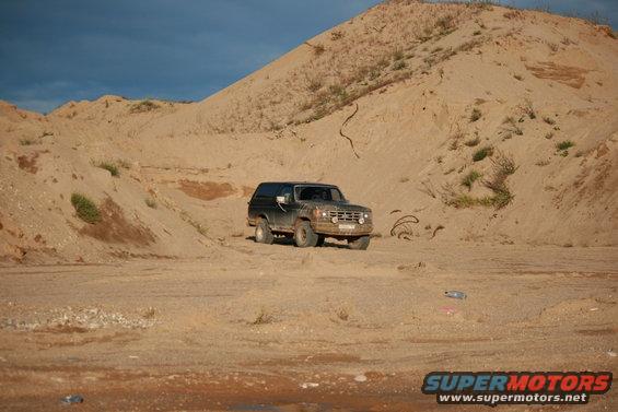 1987 Ford Bronco parked in a sandy area with hills in the background