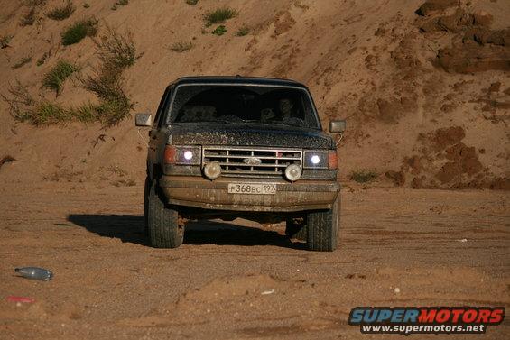 Front view of a black 1987 Ford Bronco driving on a sandy terrain