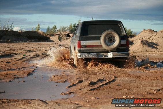1987 Ford Bronco driving through mud, spare tire mounted on rear door