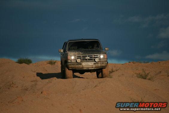 1987 Ford Bronco driving on sand dunes under a dark sky