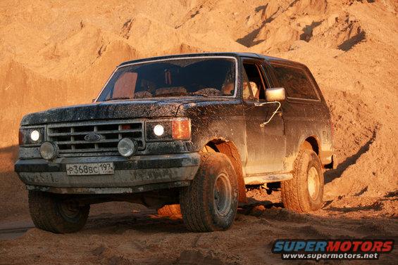 Black 1987 Ford Bronco driving on sand, front 3/4 view