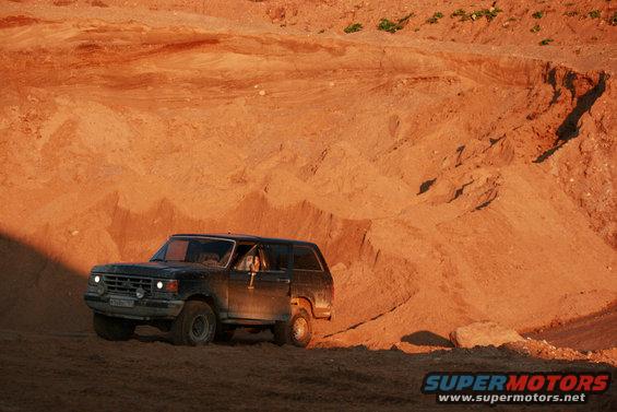 1987 Ford Bronco driving on a sandy hill, driver visible through window