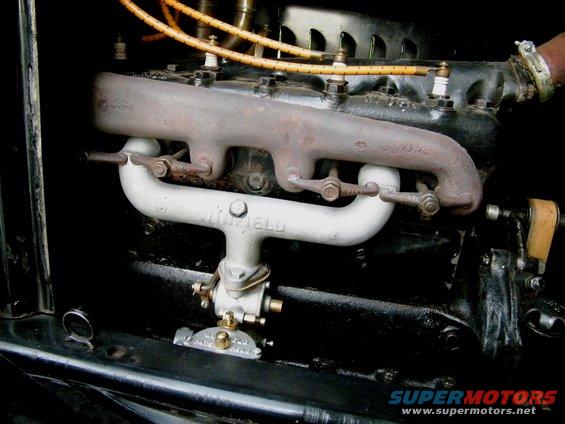 Close-up of an engine with a Winfield carburetor and exhaust manifold. Spark plug wires are visible