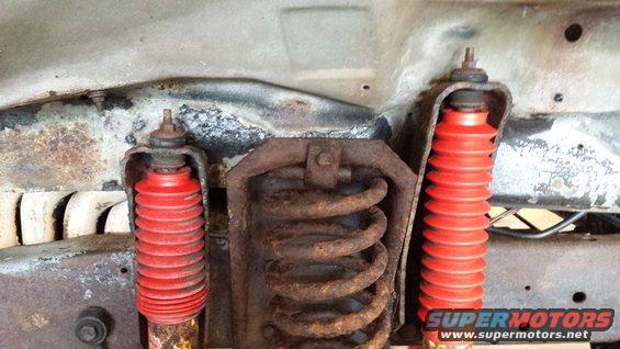 Undercarriage view of red shock absorbers and rusty coil springs. Supermotors.net logo visible