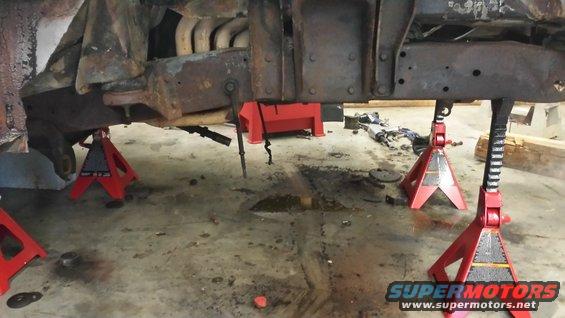 Vehicle frame supported by red jack stands in a garage, with exhaust pipes visible