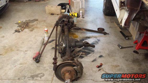Front axle assembly with red shock absorber and brake components on concrete floor