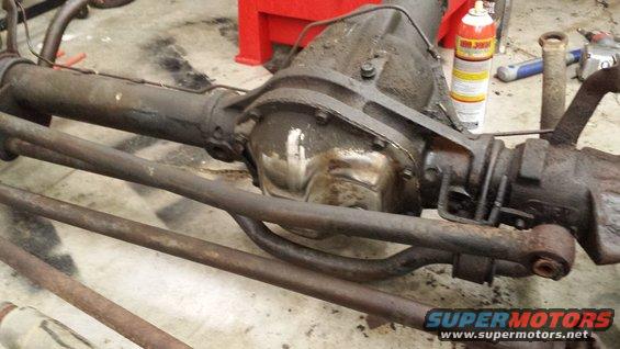 Vehicle's rear axle assembly with steering linkage and suspension components. It's dirty and appears to be in a workshop