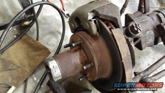 close-up of a rusty vehicle brake rotor, caliper, and hub assembly