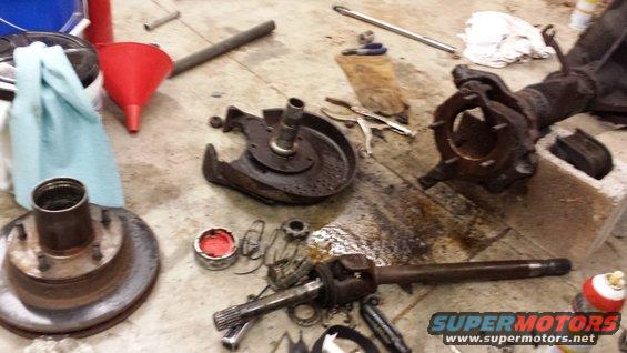 Disassembled front axle parts and brake rotor on a concrete floor