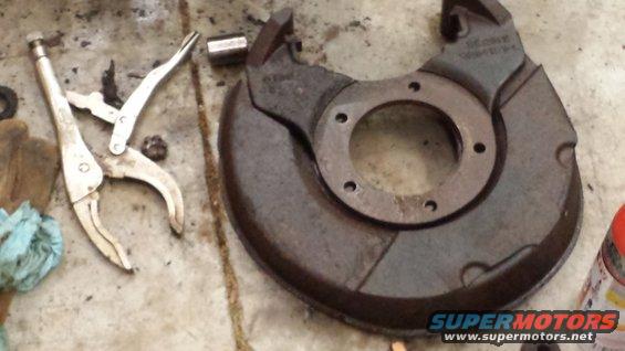 Rusty brake dust shield with vise grips and a socket on a concrete surface