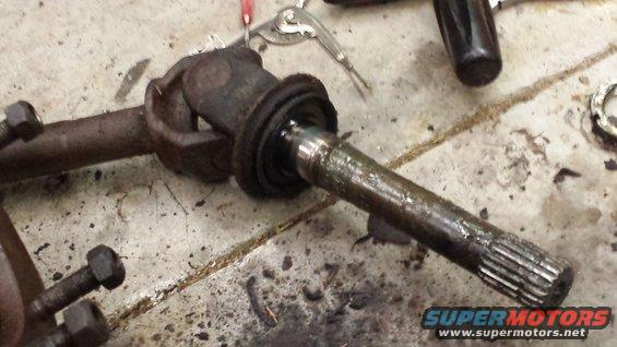Driveshaft U-joint connected to a splined axle shaft, resting on a concrete floor with tools nearby