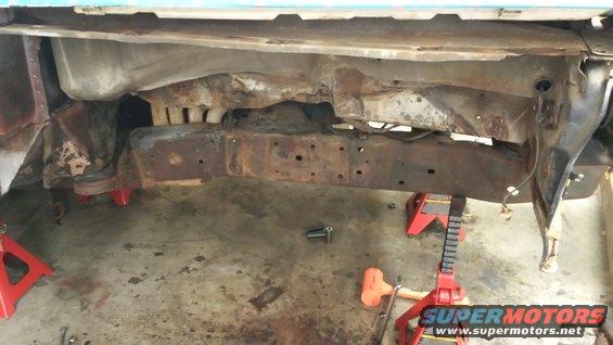 rusted frame of a vehicle on red jack stands, showing extensive rust and damage