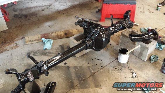 black rear axle assembly on concrete floor, paint can nearby
