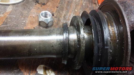 Axle shaft with black rubber seals and a lug nut on a workbench