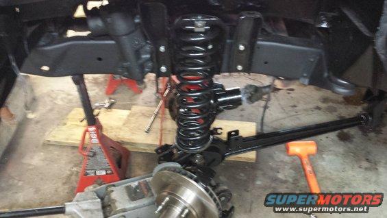 Vehicle suspension components on jack stands, with a large coil spring and brake rotor visible