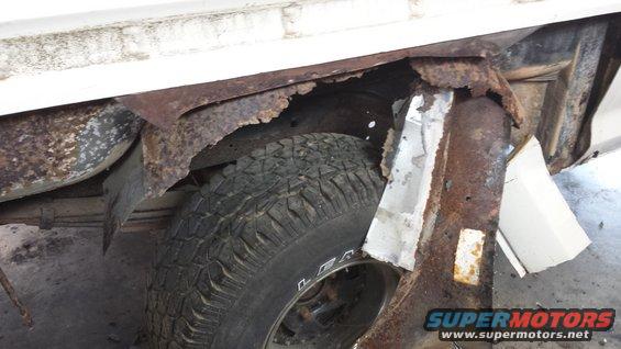 Close-up of heavily rusted metal in a vehicle's wheel well, showing a tire and part of the frame