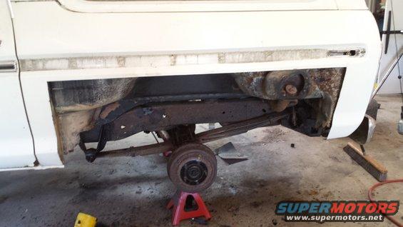White Ford Bronco with rear wheel removed, showing rusty frame and suspension components on jack stands