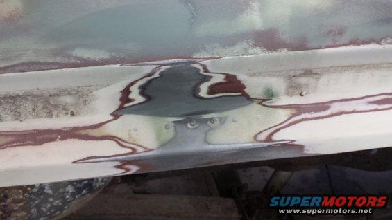 Car body panel with visible body filler and primer layers, showing repair work