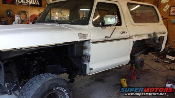 White 1978 Ford Bronco with front fender removed, sitting on jack stands in a garage