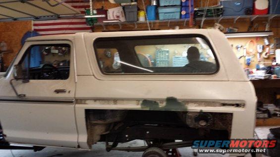 1978 Ford Bronco side view in a garage, undergoing restoration with the lower body panel removed