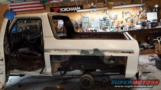 White Ford Bronco body in a garage, doors open, missing fenders and bed