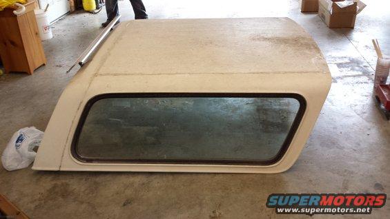 White truck cap with a large side window, resting on a concrete floor