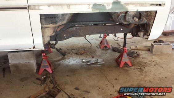 Vehicle frame on jack stands, with concrete blocks and tools on the floor