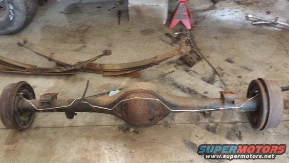 Rusty rear axle assembly with brake drums and leaf springs on a concrete floor