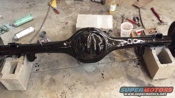 Black rear axle assembly on cinder blocks, with spray cans and tools nearby