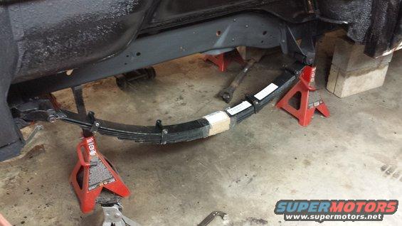 Vehicle frame supported by jack stands, showing a leaf spring assembly. Some tape is wrapped around the spring