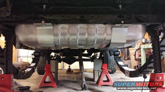 Undercarriage of a vehicle on jack stands, showing a large fuel tank and leaf springs