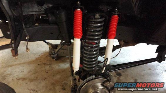Vehicle suspension with red and white shocks, large coil spring, and brake rotor